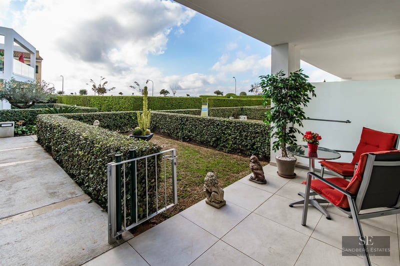 Modern white terrace with two red chairs and table overlooking a private garden with perfectly trimmed hedges.