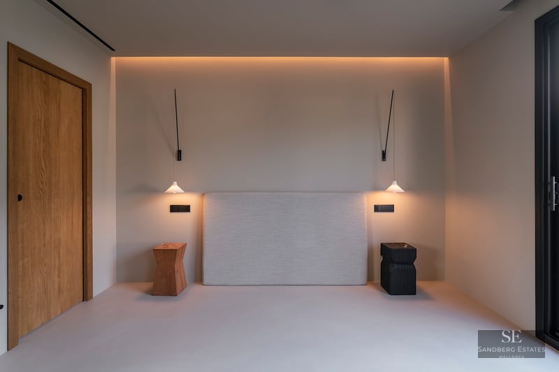 Tête de lit rembourrée entre des suspensions et des tabourets en bois sous un éclairage chaleureux et indirect.