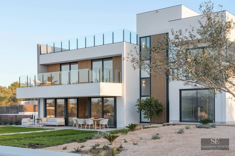 Two-story modern white villa with glass balconies, wooden slats, outdoor dining area, and a rooftop terrace.