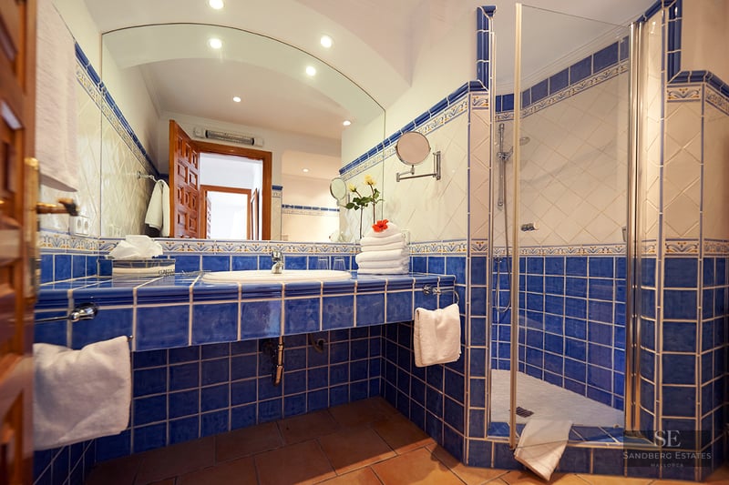Blue and white tiled bathroom featuring a large arched mirror and a glass walk-in shower.