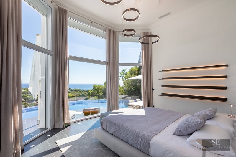 Modern master bedroom with floor-to-ceiling windows overlooking an infinity pool and the Mediterranean sea.