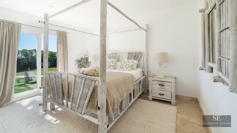 Bright bedroom featuring a white bamboo canopy bed, woven textures, and direct garden access via glass doors.
