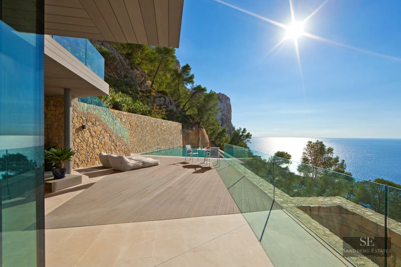 Modern villa terrace with infinity pool, wooden decking, glass railings, and panoramic views of the Mediterranean Sea.