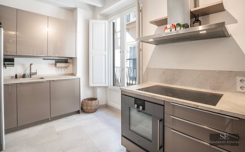 Bright modern kitchen with taupe glossy cabinets, stone countertops, integrated oven, and a balcony door.