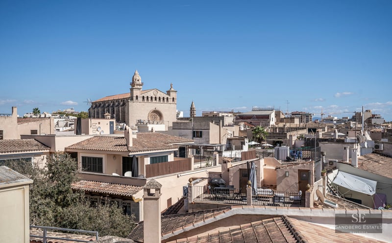 Vue surélevée de toits traditionnels en terre cuite et d'une majestueuse cathédrale en pierre sous un ciel bleu clair.