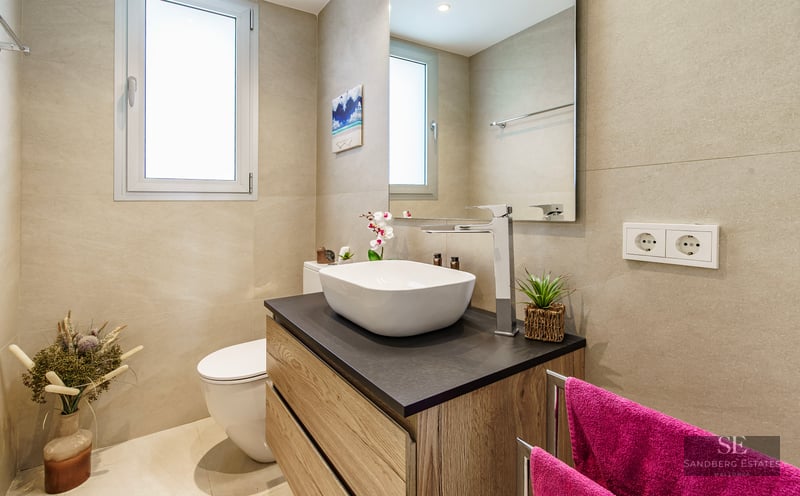 Modern bathroom featuring a white vessel sink on a wood vanity, a large mirror, and beige tiled walls.