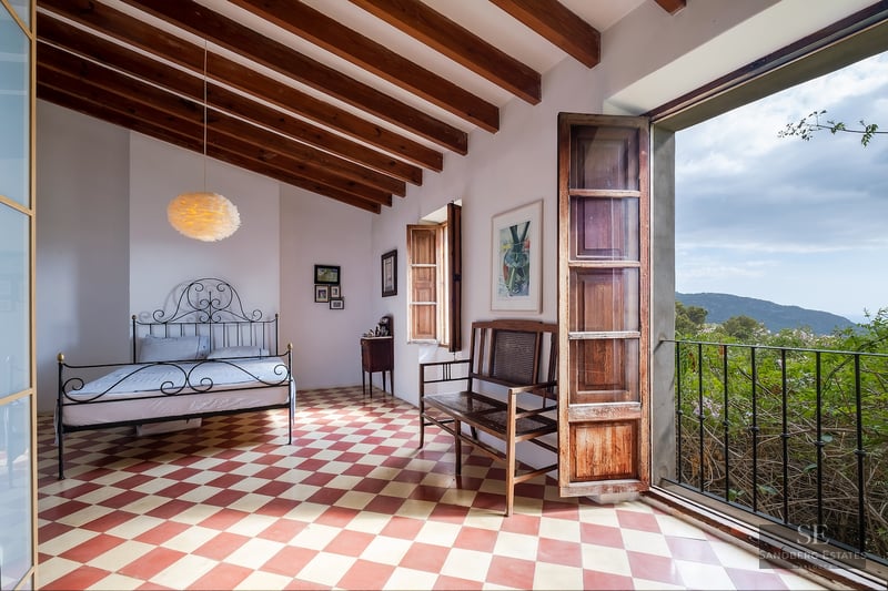 Bedroom featuring a checkered floor, wrought iron bed, wood-beamed ceiling, and an open door viewing lush mountains.