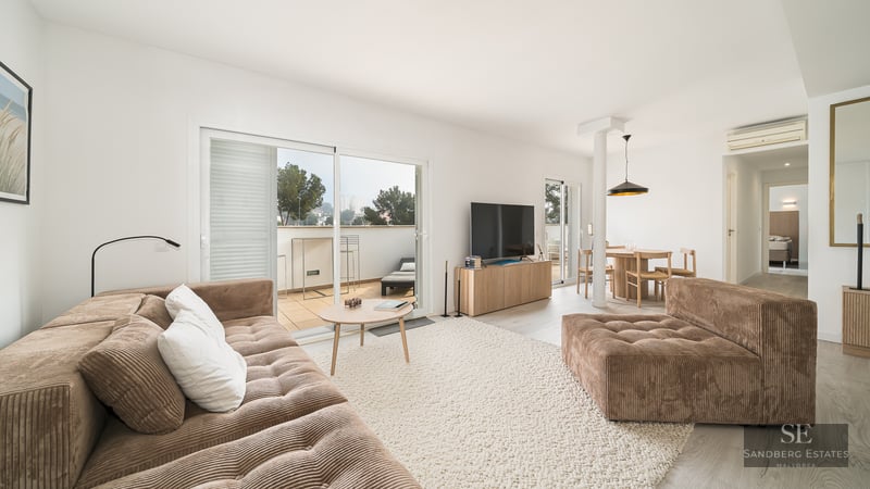 Modern living room with a brown corduroy sofa, large rug, and sliding glass doors leading to a sunlit terrace.