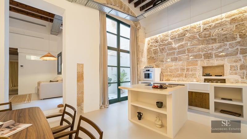 Minimalist kitchen featuring a large natural stone wall, white island, and high ceilings with wooden beams.