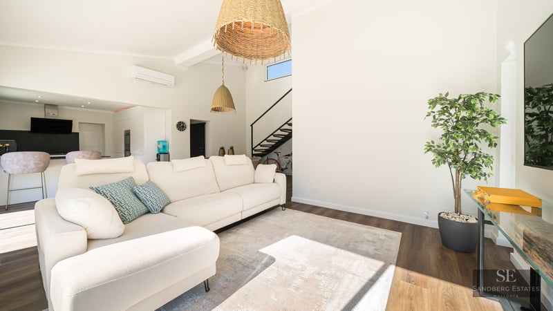 Salon spacieux avec canapé d'angle blanc, luminaires en rotin et parquet foncé.