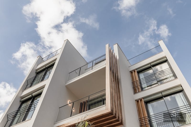 Low-angle view of a modern white building facade with wooden accents and black railings against a blue sky.