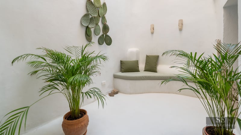 Banquette courbée en maçonnerie blanche avec coussins verts dans un patio minimaliste entouré de palmiers en pots.