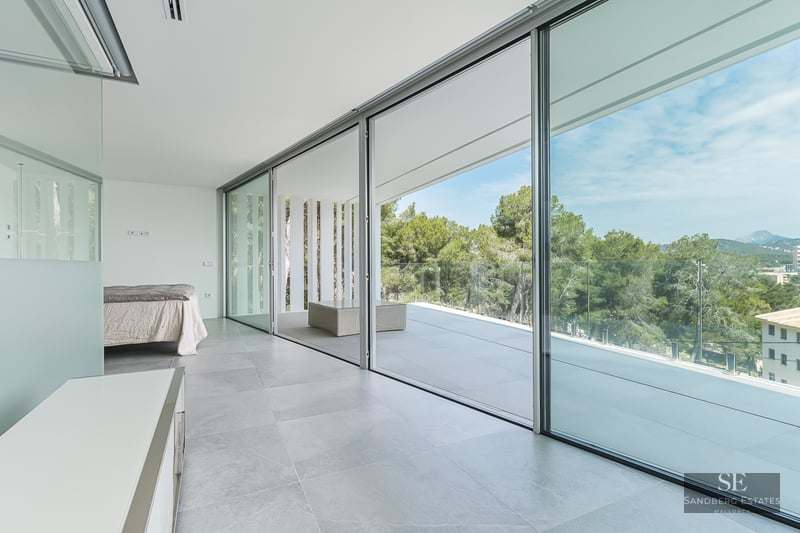 Bright minimalist bedroom with large sliding glass doors opening to a terrace with forest views.
