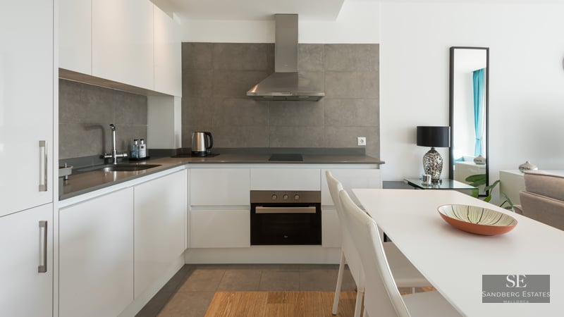 Cuisine blanche moderne avec crédence grise, appareils en inox et table à manger blanche.