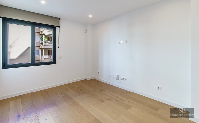 Pièce vide et lumineuse avec parquet en bois clair, murs blancs et une grande fenêtre avec store.