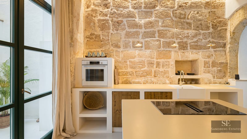 A modern kitchen with an exposed stone wall, white cabinetry, wooden accents, and a kitchen island.