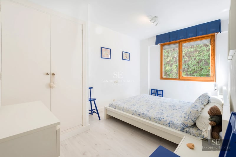 Spacious balcony with glass railing and sea view. Modern outdoor furniture. Sand-colored tile floor. Soft lighting.