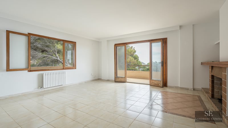 Empty living room with tiled floors, a fireplace, wooden window frames, and glass doors leading to a balcony.