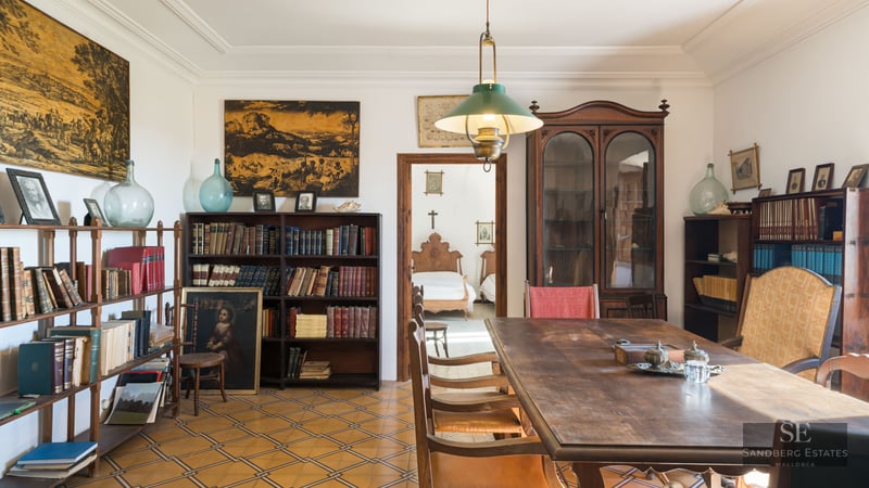A classic room featuring a large wooden table, floor-to-ceiling bookshelves, and patterned tile flooring.