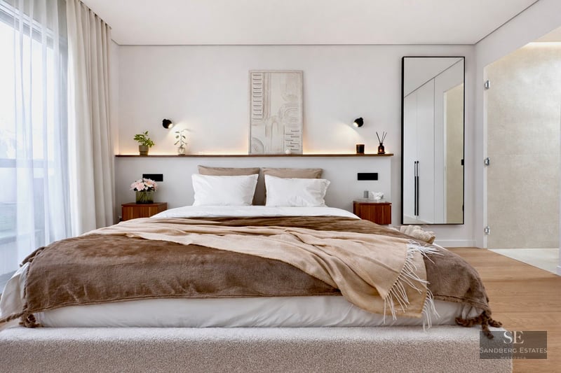 Bright master bedroom with a large bed, brown bedding, wooden nightstands, and integrated shelf lighting.