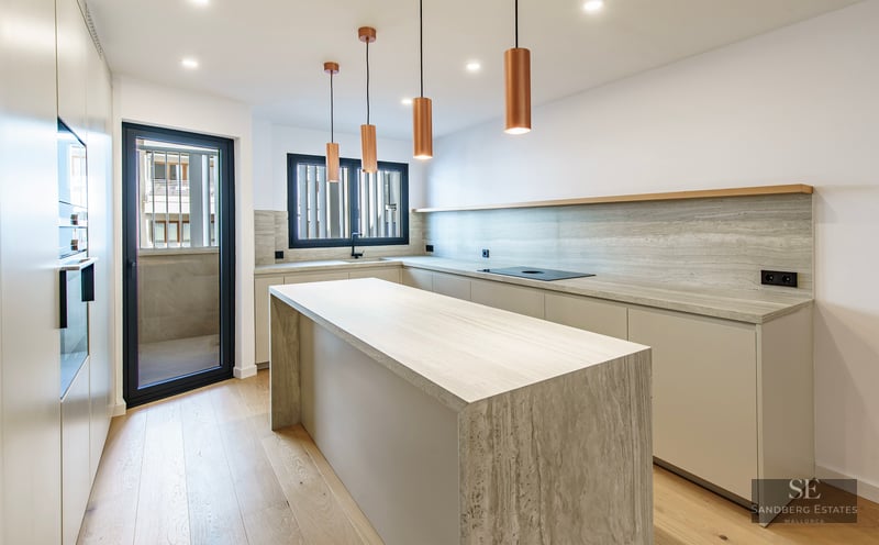 Cuisine lumineuse avec îlot en travertin, suspensions en cuivre et parquet en bois clair.