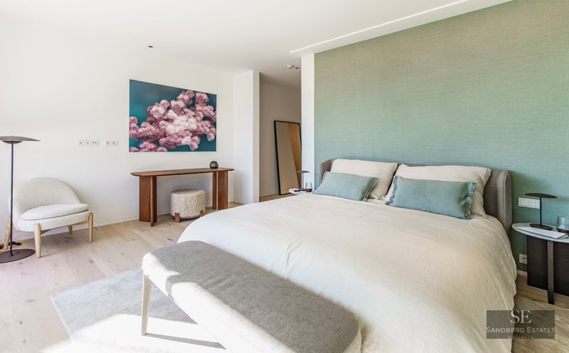 Bright master bedroom featuring a sage green wall, large bed, and designer furniture on light wood floors.