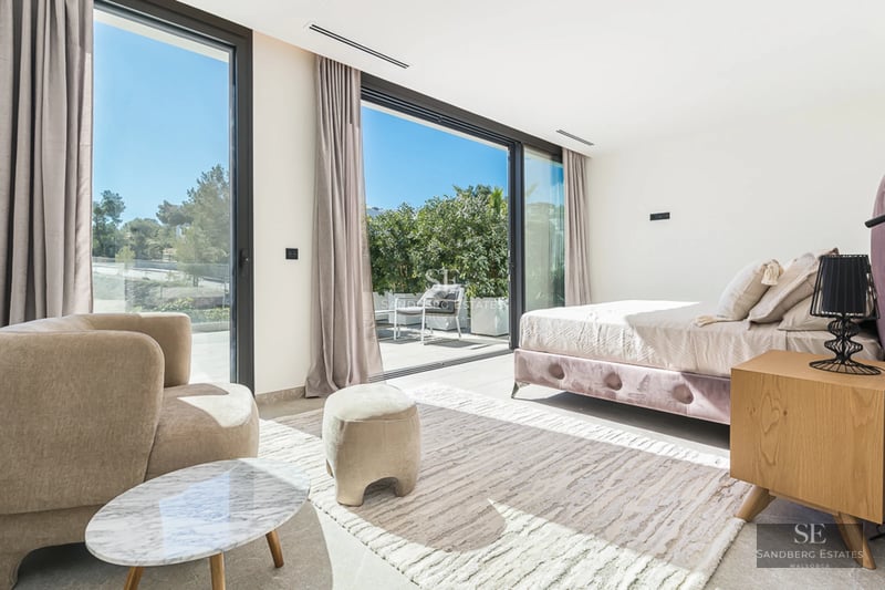 Vaste piscine bordée de carreaux clairs et de chaises longues. Villa moderne avec de grandes baies vitrées et une végétation luxuriante.