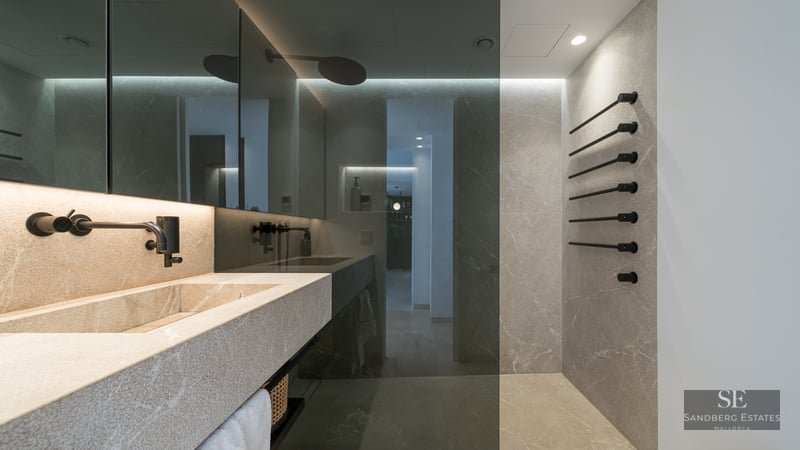 Modern bathroom with a stone sink, matte black faucet, and stone tiled walls with a glass shower screen.