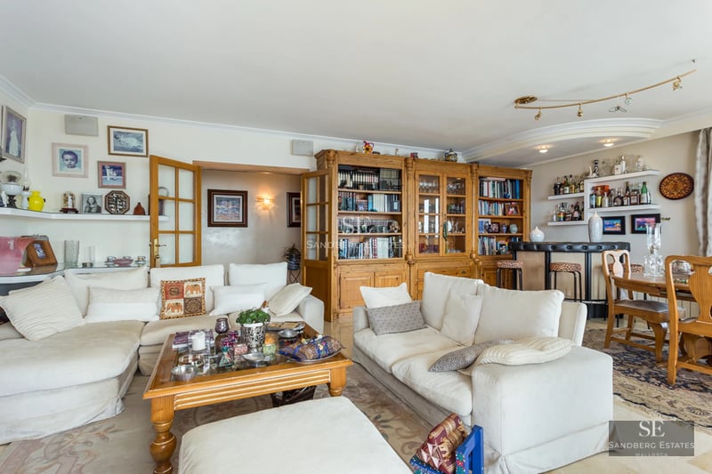 Large living room with white sofas, a massive wooden bookcase, a home bar area, and a dining table.