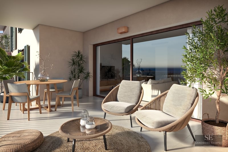 Modern terrace with woven lounge chairs, wooden dining table, and large glass doors reflecting a sea view.