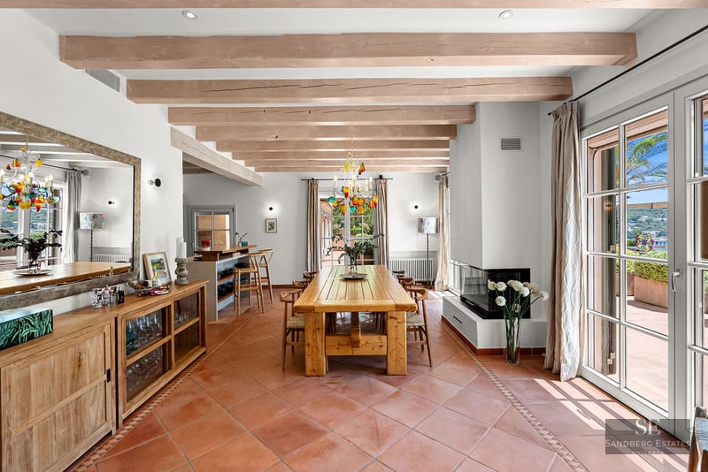Large dining area featuring a wooden table, terracotta tile floors, exposed ceiling beams, and terrace access.