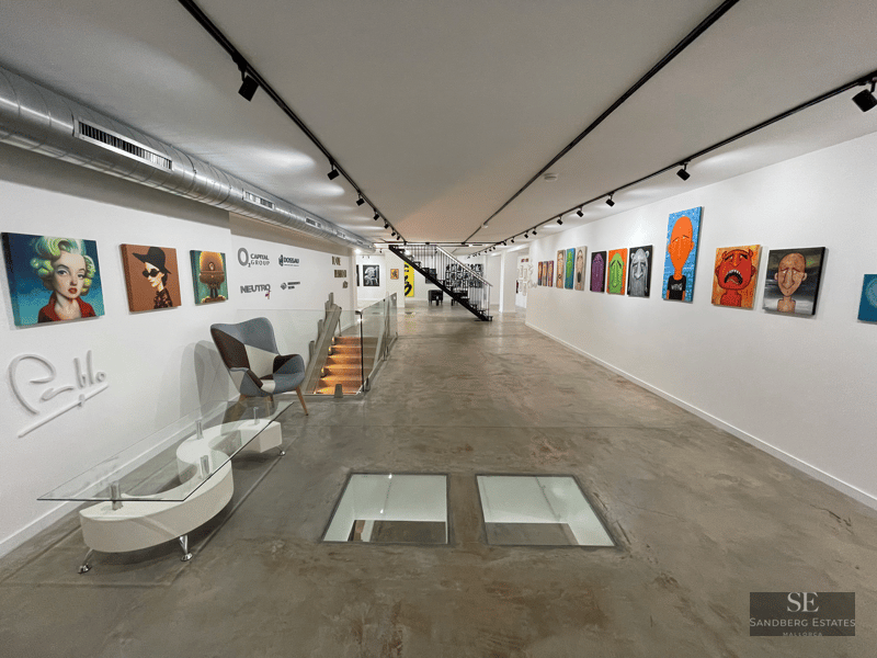 A long industrial gallery with polished concrete floors, white walls filled with pop art, and glass floor inserts.