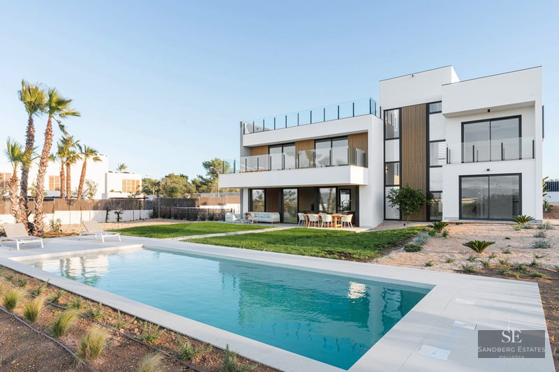 Modern white design villa featuring a rectangular swimming pool, manicured lawn, and spacious terraces under a clear sky.
