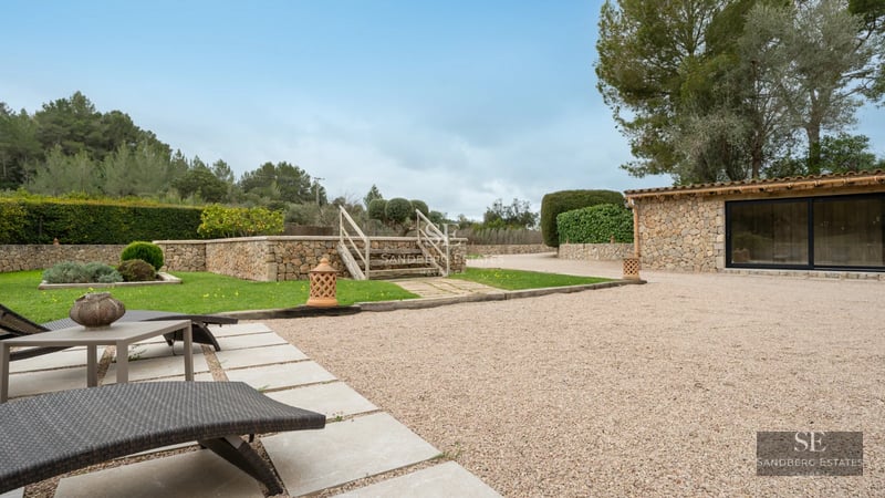 Exterior view of a modern villa featuring a pool, garden, and expansive glass windows reflecting the blue sky.
