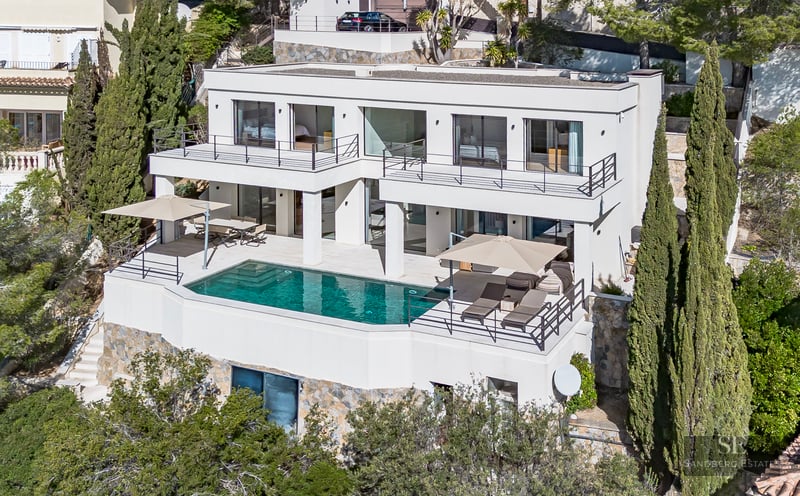 Elevated view of a white multi-level modern villa with a turquoise swimming pool on a stone terrace.