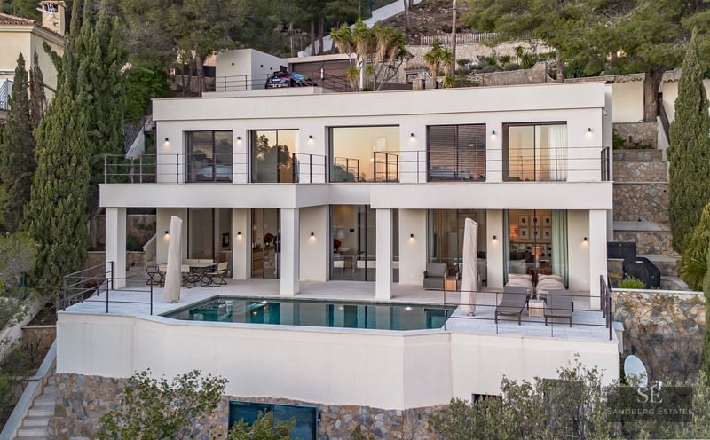 Modern white two-story villa on a hillside with a rectangular pool and multiple terraces at dusk.