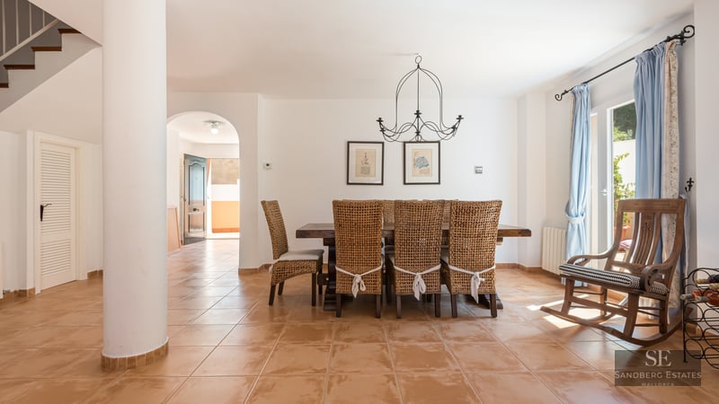 Dining room featuring a large wooden table, wicker chairs, terracotta tile floor, and a wooden rocking chair.