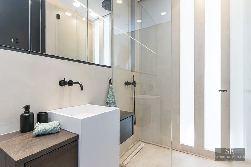Modern bathroom featuring a white square vessel sink, black wall-mounted faucet, and a glass-enclosed shower.