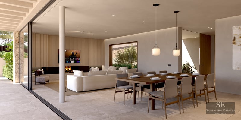 Modern open-plan room with large dining table, white sectional sofa, fireplace, and floor-to-ceiling glass doors.