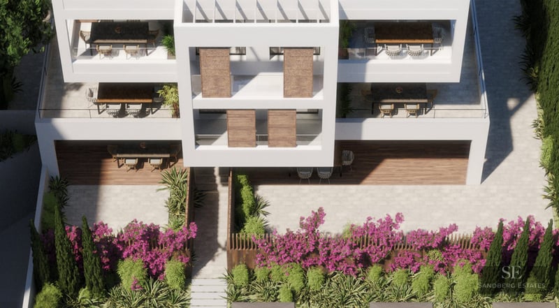 High-angle view of a white modern apartment building with wooden shutters, terraces, and a garden with purple flowers.