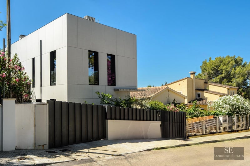Exterior of a modern white design house with black fencing and clear blue sky.
