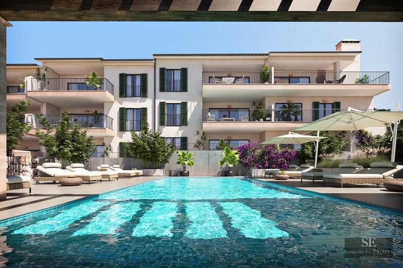 Outdoor swimming pool with sun loungers in front of a modern Mediterranean building with balconies and green shutters.