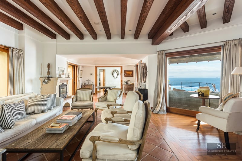 Grand balcon avec vue sur mer depuis un appartement moderne. Garde-corps en verre, plancher en bois et mobilier extérieur élégant.