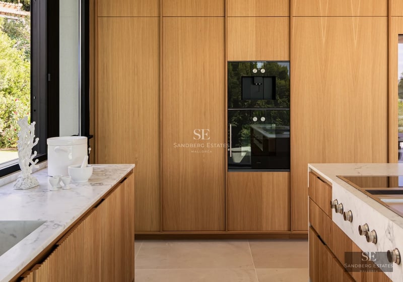 View of a modern villa with an infinity pool, wooden terrace, and large windows overlooking the sea. Minimalist design with high-end finishes.