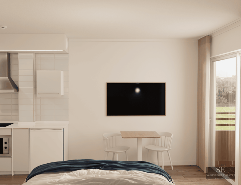 Studio lumineux avec lit, kitchenette, table à manger, télévision et porte-fenêtre.