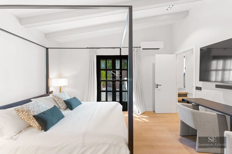 View of a luxurious pool with loungers and umbrellas, surrounded by gardens and a modern house in the background.