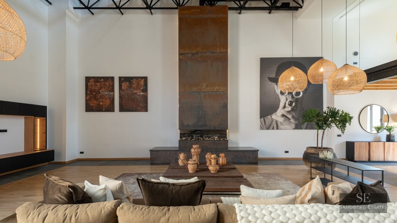 Spacious living room with a tall weathered steel fireplace, beige sofa, and woven pendant lamps in an industrial loft.