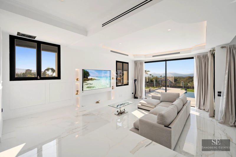 Spacious balcony with panoramic sea views. Glass railing, modern outdoor furniture, wooden floor, and lush vegetation.