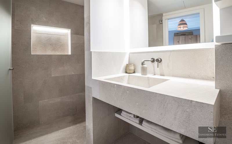 Salle de bain moderne en pierre avec vasque intégrée, robinet mural et niche murale éclairée.