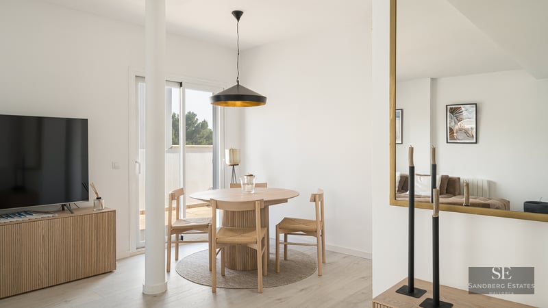 Bright dining area featuring a round wooden table, wicker chairs, black pendant lamp, and terrace access.